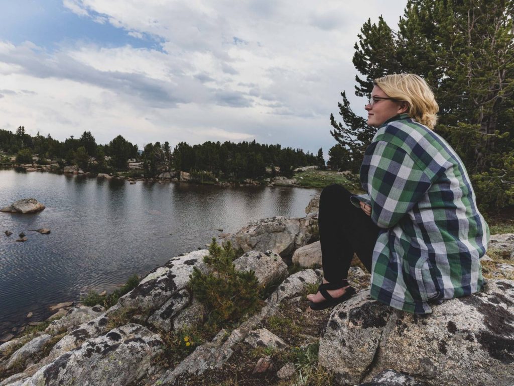 Teenage girl sitting on rock next to lake