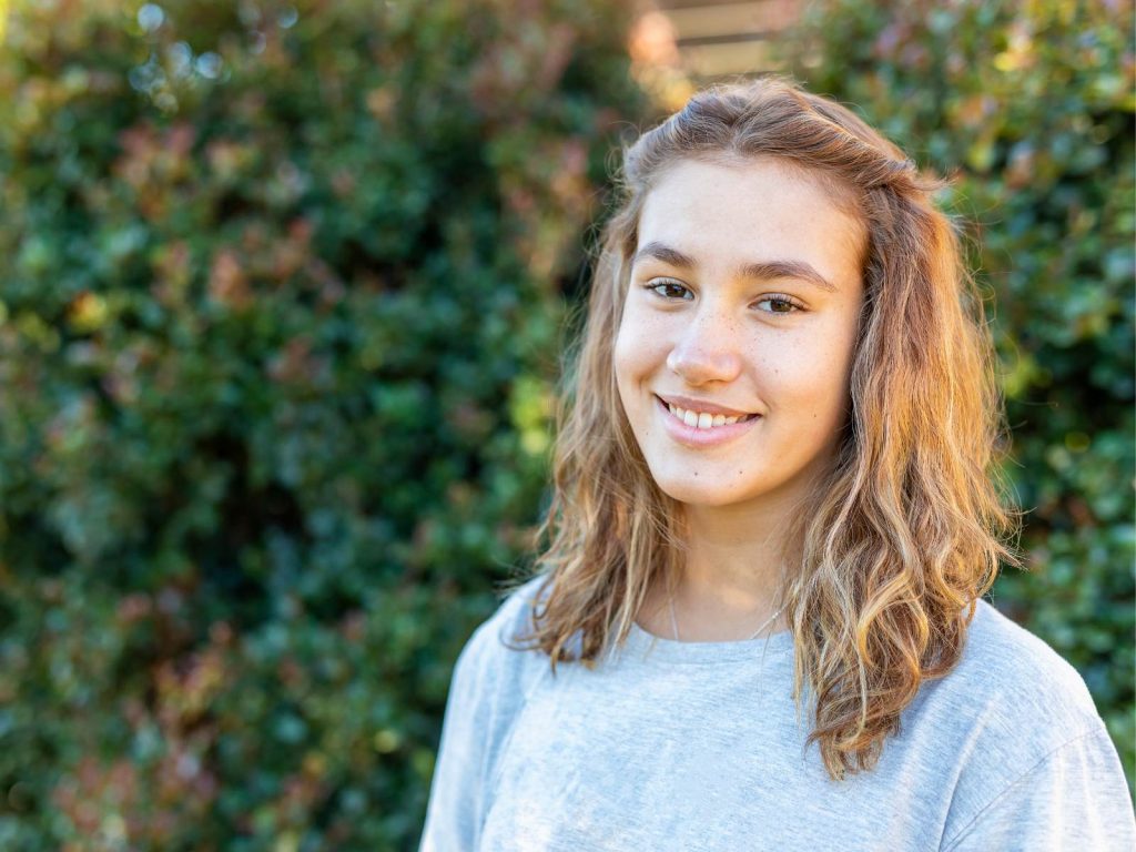 Teenager girl smiling in front of bushes